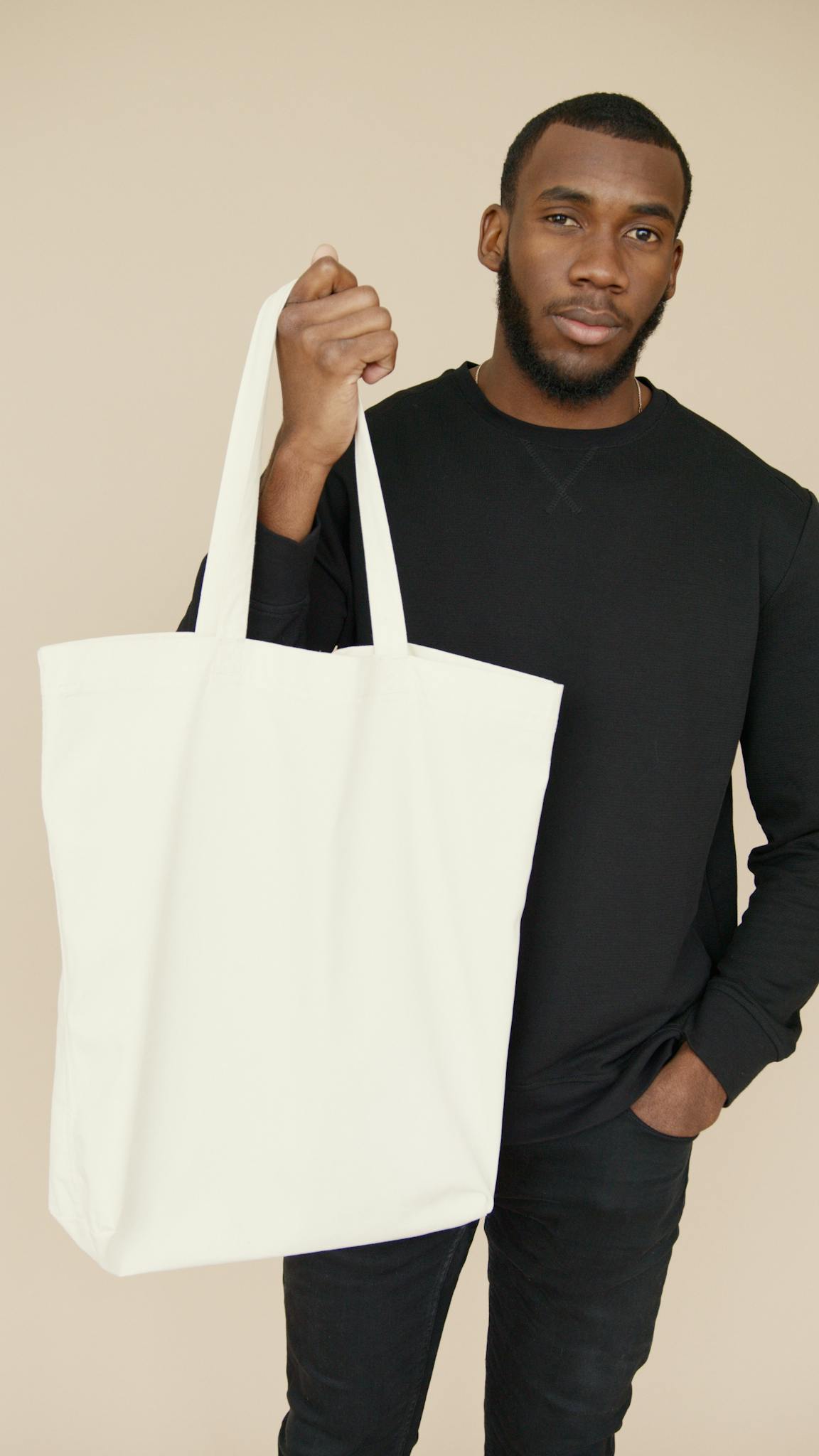 FAQ Portrait of a young man holding a blank white tote bag, ideal for mockup and branding purposes.